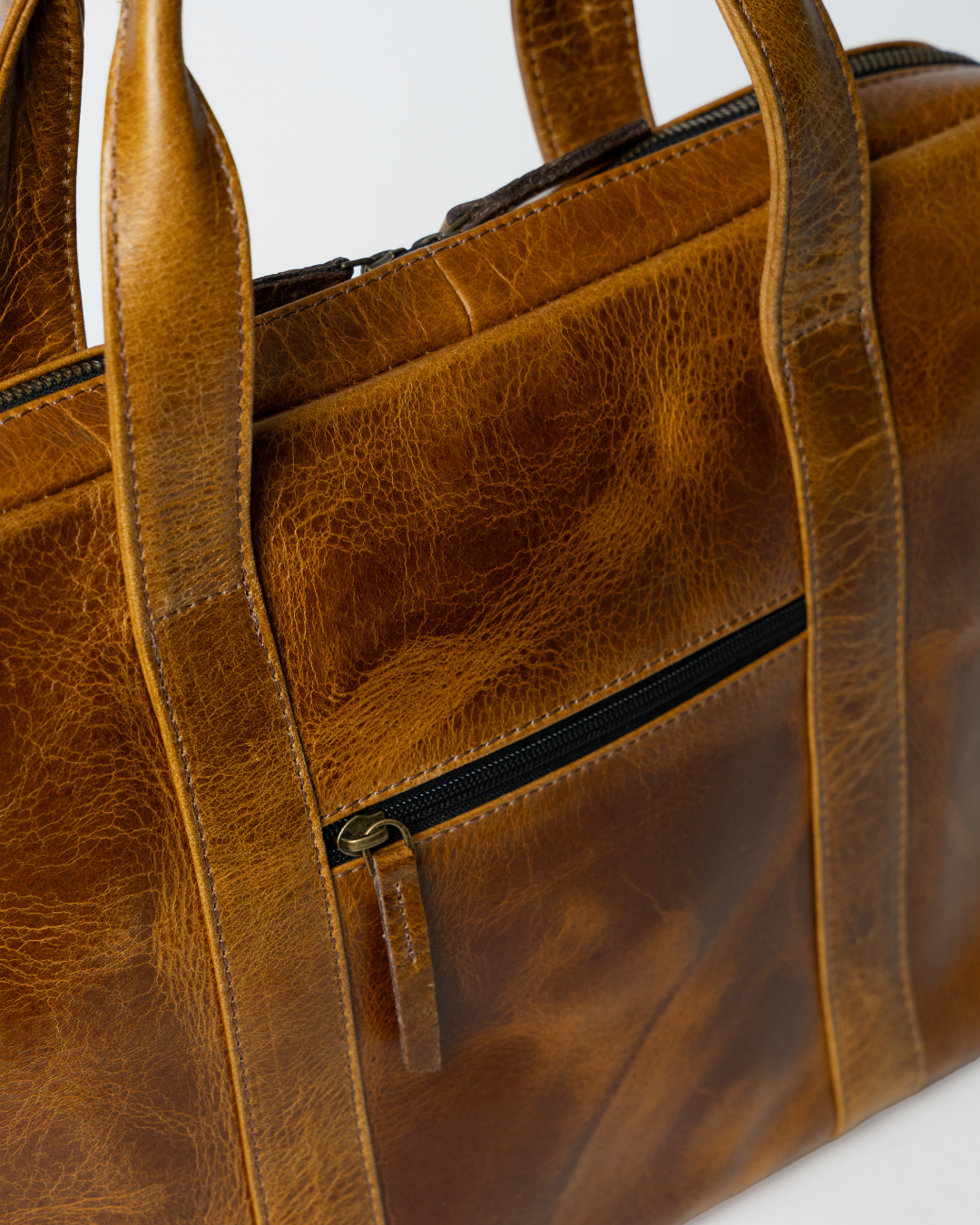Close-up of the Laylowe Nolan light brown leather laptop case showing its front zip pocket, leather grain and handles.