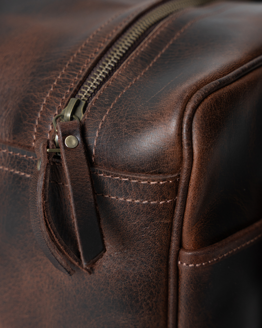 Close-up of the Laylowe Holden dark brown leather travel bag showing the top zipper, leather pull and stitching.