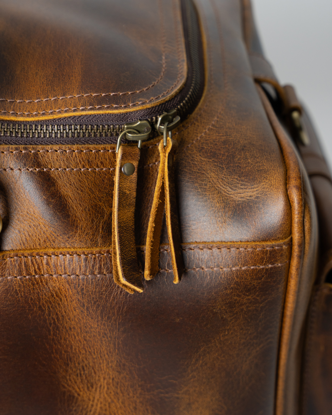 Close-up of the Laylowe Alden brown leather weekender showing twin leather zipper pulls and stitched trim.