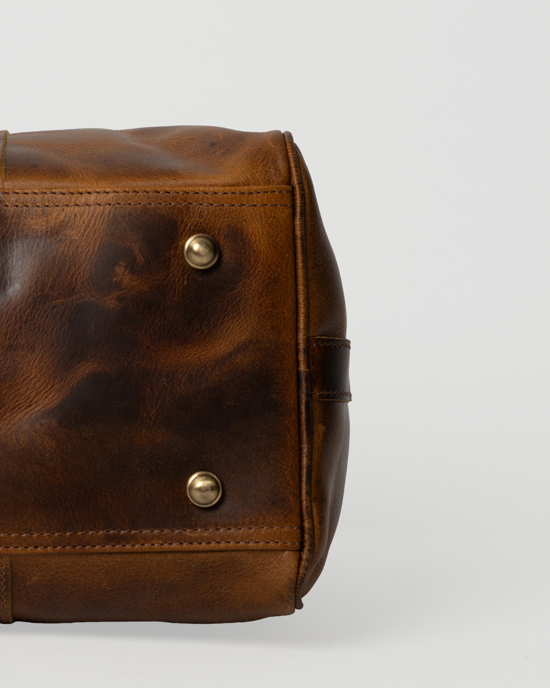 Underside detail of the Laylowe Beck light brown small leather duffle showing metal feet and stitched leather base.