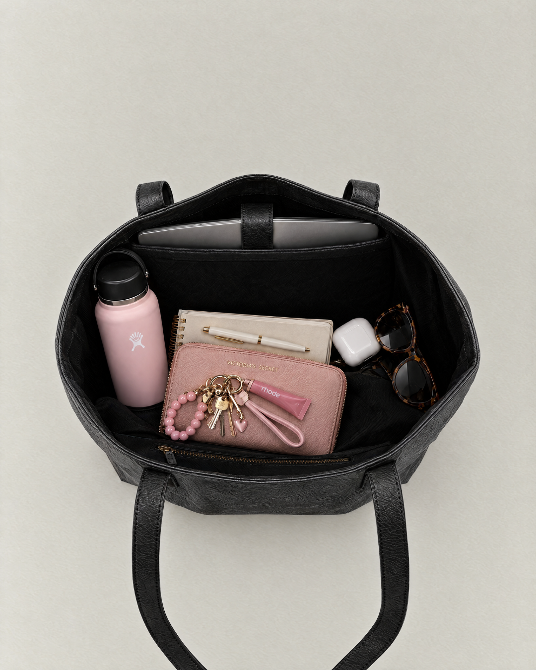 Top view of a Laylowe Arden black leather work tote packed with a laptop, bottle, notebook, wallet and sunglasses.