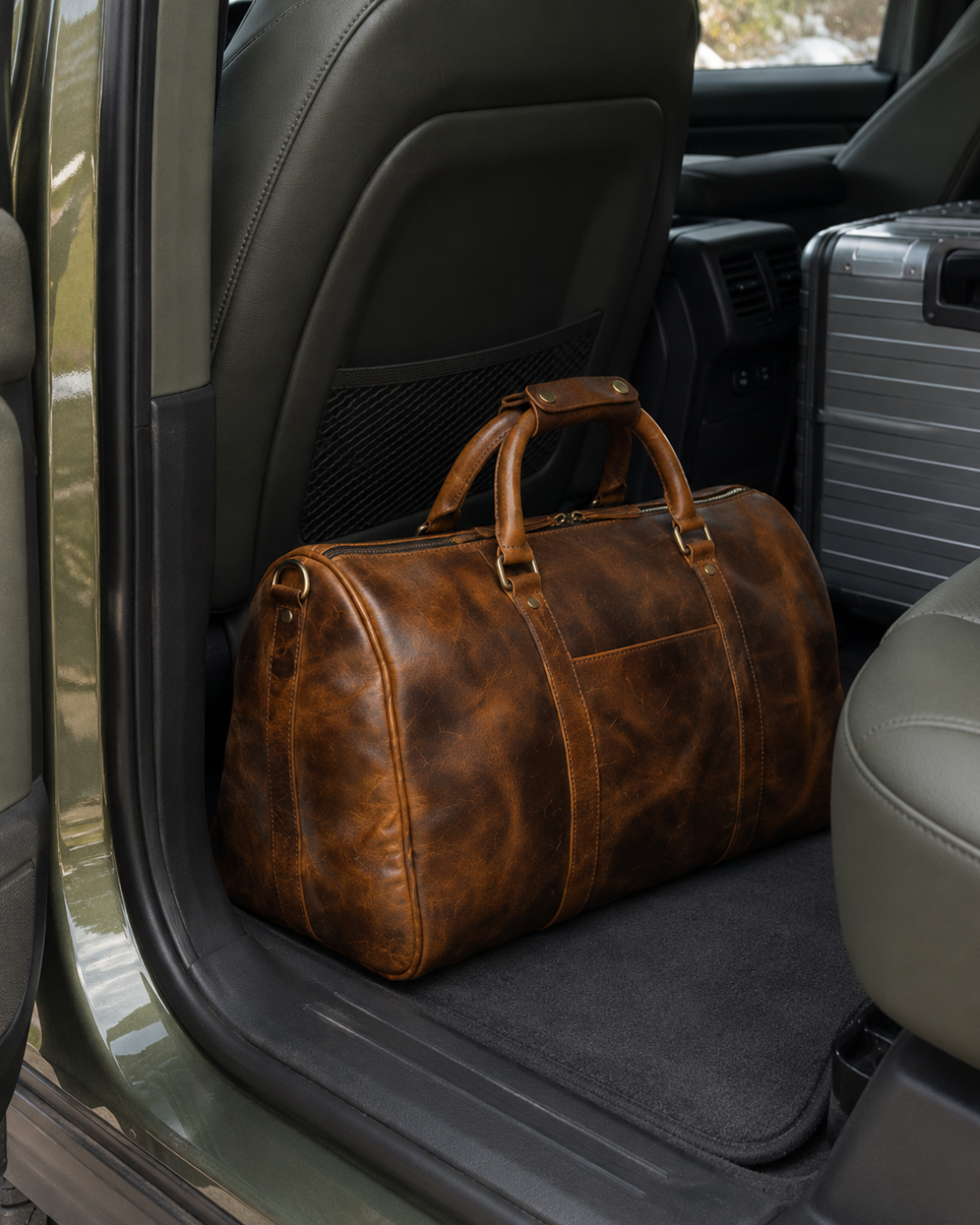 Laylowe Beck light brown small leather duffle in a car footwell beside a silver suitcase.