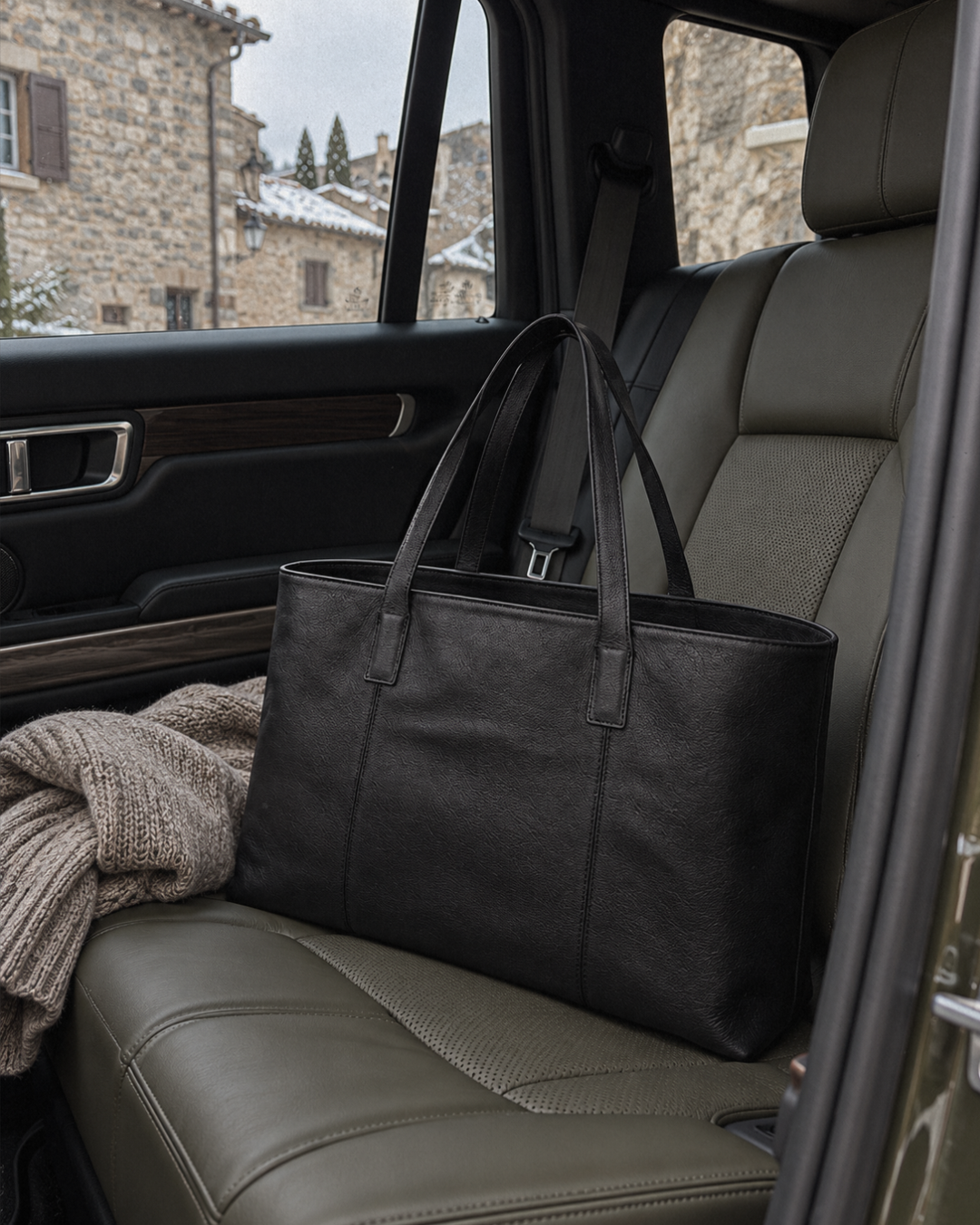 Laylowe Arden black leather tote bag on a car passenger seat beside a folded knit.