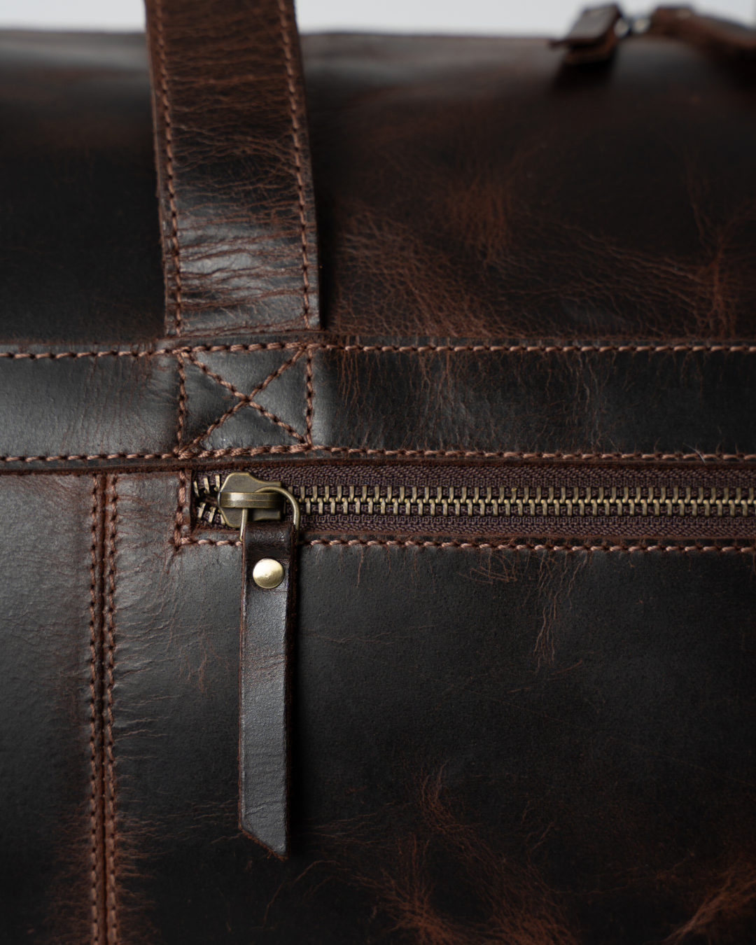 Close-up of the Laylowe Rowan dark brown leather duffle showing the front zip pocket and stitched handle attachment.