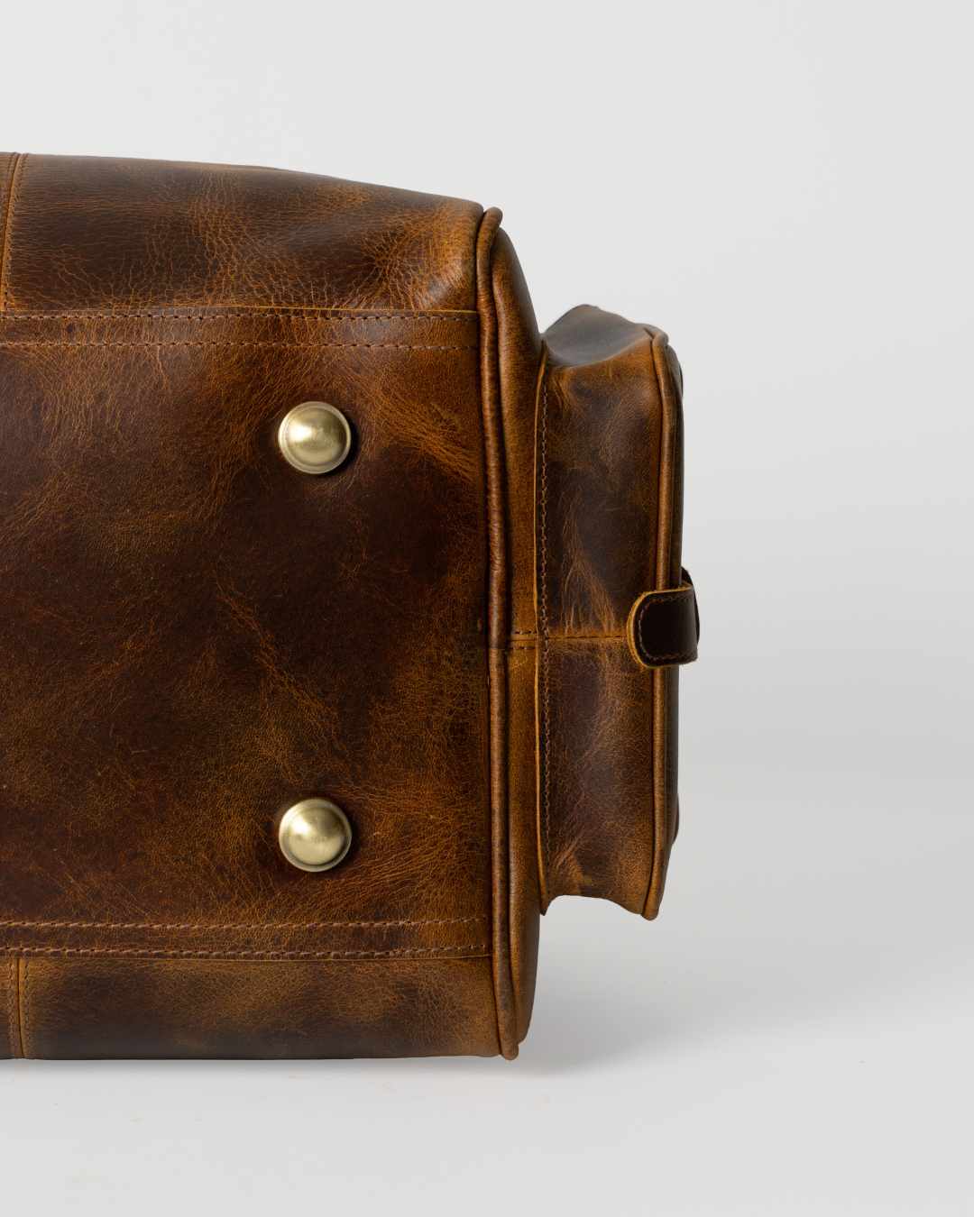 Underside detail of the Laylowe Alden brown leather weekender showing metal feet, stitching and a side pocket.
