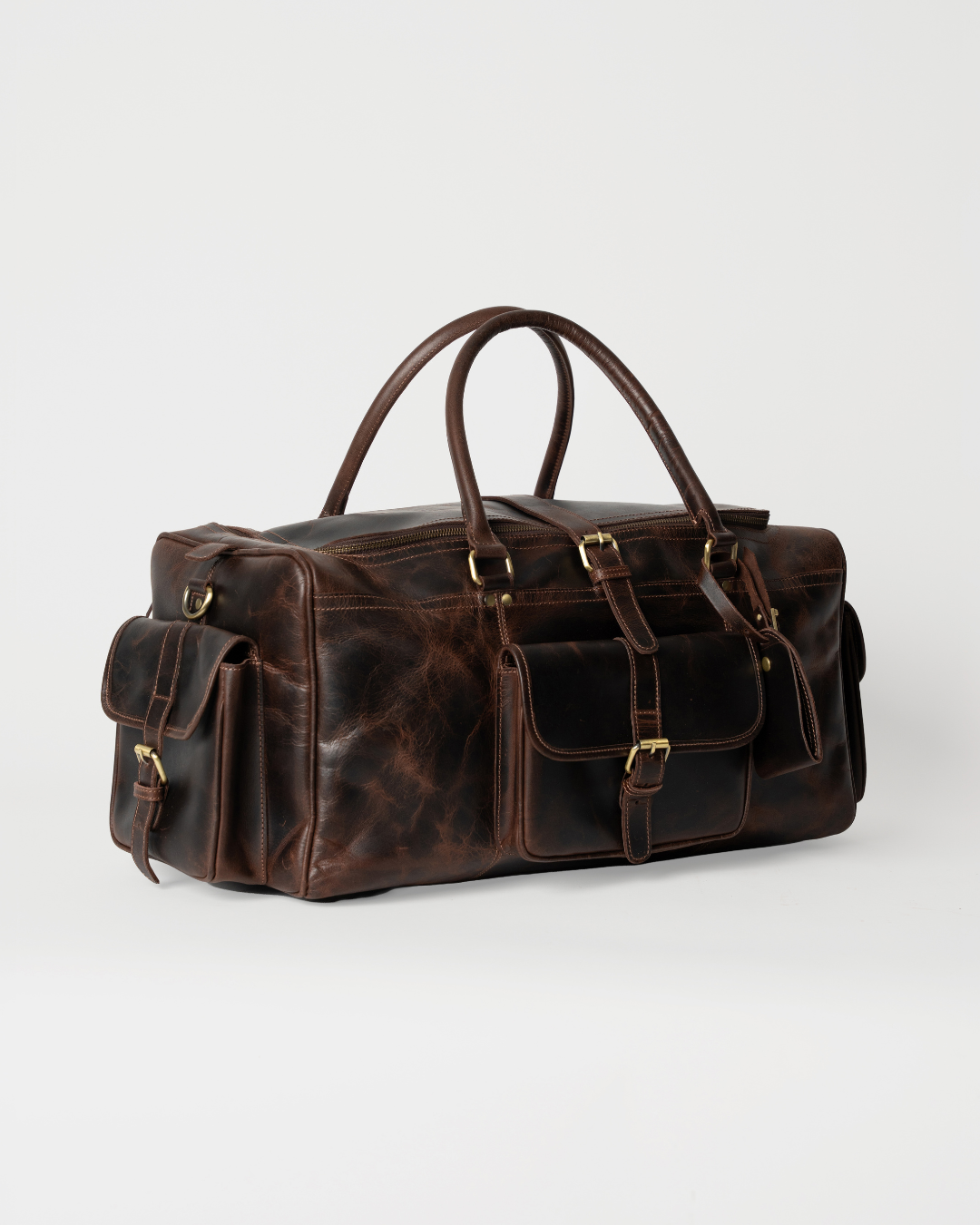 Laylowe Bennett dark brown leather travel bag, three-quarter view showing front and end flap pockets with buckles.