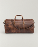 Rear view of the Laylowe Rhodes light brown leather travel bag with its shoulder strap draped across the leather panels.