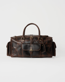 Laylowe Bennett dark brown leather travel bag, front view with a buckled flap pocket, rolled handles and end pockets.