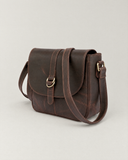 Angled view of the Laylowe Cora dark brown leather satchel showing the flap, buckle and side strap attachment.