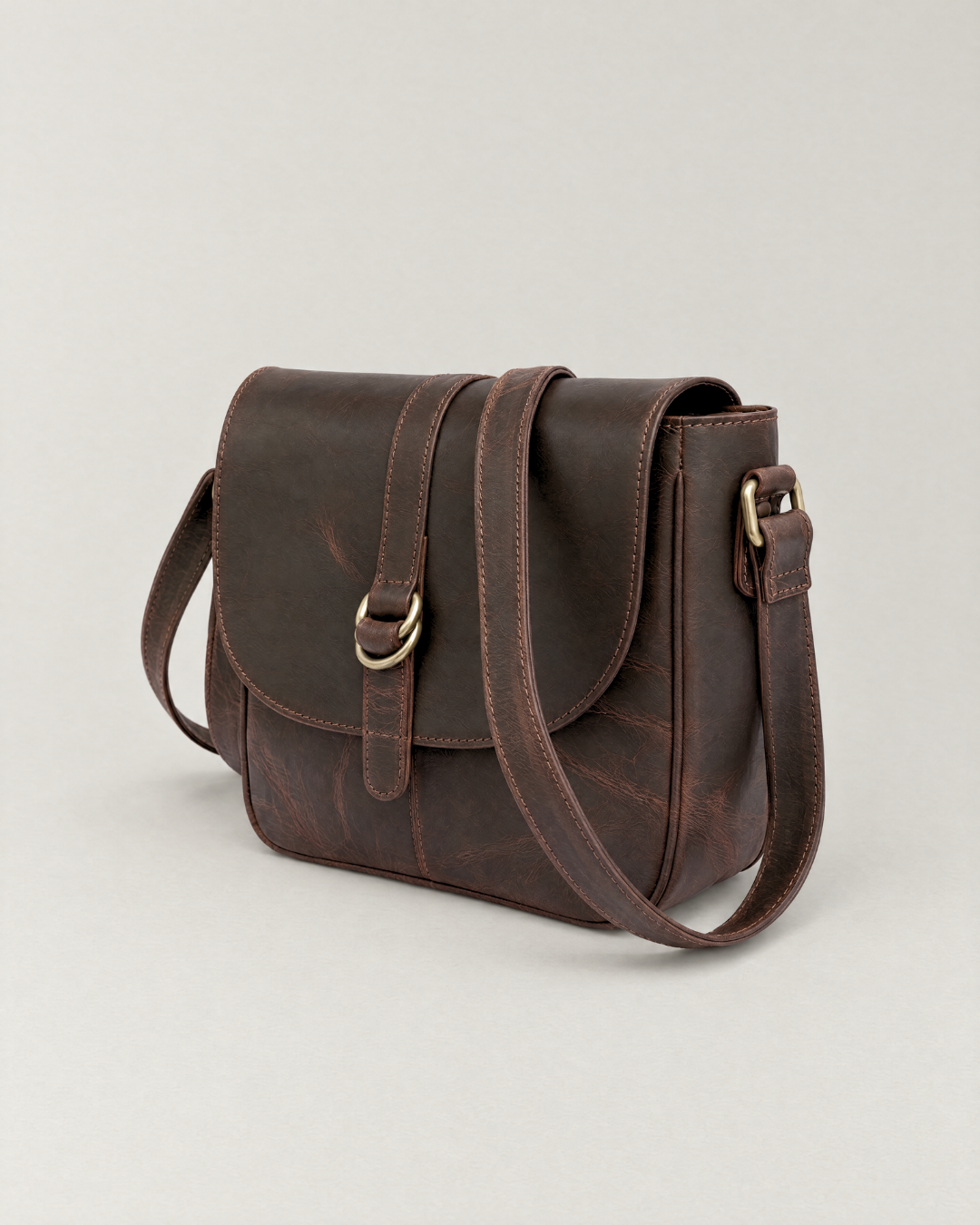 Angled view of the Laylowe Cora dark brown leather satchel showing the flap, buckle and side strap attachment.