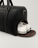 Laylowe Blake black leather duffle with its separate side shoe compartment open and holding white sneakers.
