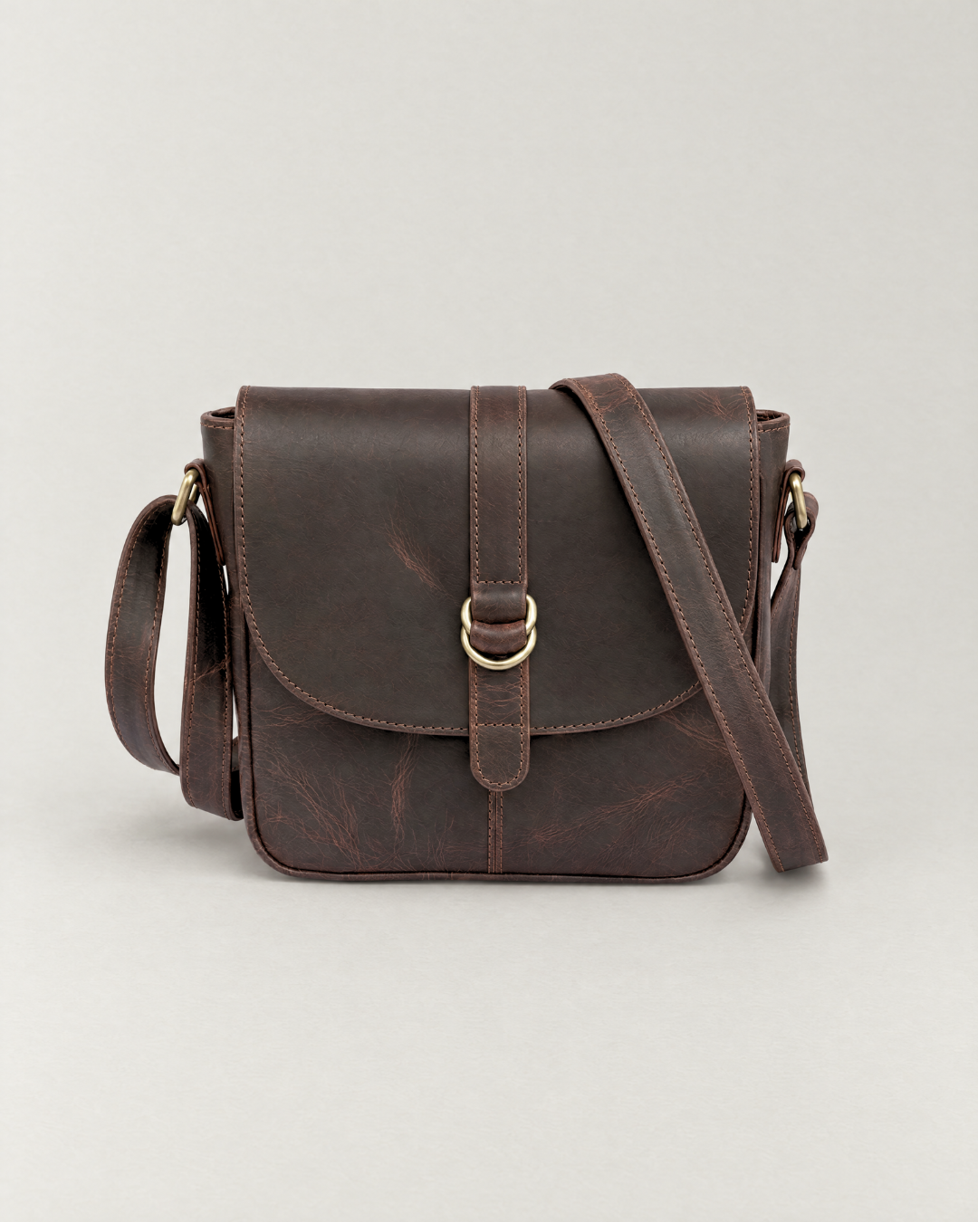Front view of the Laylowe Cora dark brown leather satchel with its rounded flap and central ring buckle.