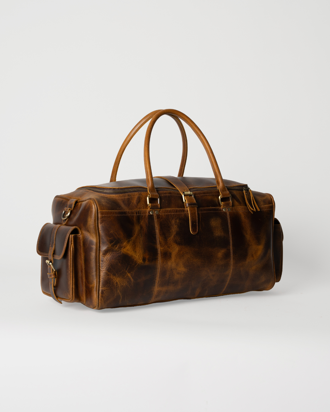 Laylowe Alden brown leather weekender, angled view showing rolled handles, mottled grain and buckled end pockets.