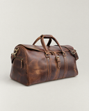 Laylowe Rhodes large light brown full-grain leather travel bag with rolled handles, a buckled flap and shoulder strap.