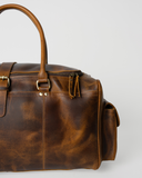 Laylowe Alden brown leather weekender close-up showing a rolled handle attachment, zipper pulls and mottled grain.