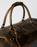 Top detail of the Laylowe Hayes light brown leather weekender, showing carry handles, zipper pulls and luggage tag.