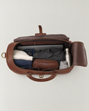 Open Laylowe Parker tan leather weekender packed with a laptop, passport, clothes, toiletry pouch and metal bottle.