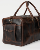 Angled end detail of the Laylowe Holden dark brown leather travel bag showing the flap pocket and strap ring.