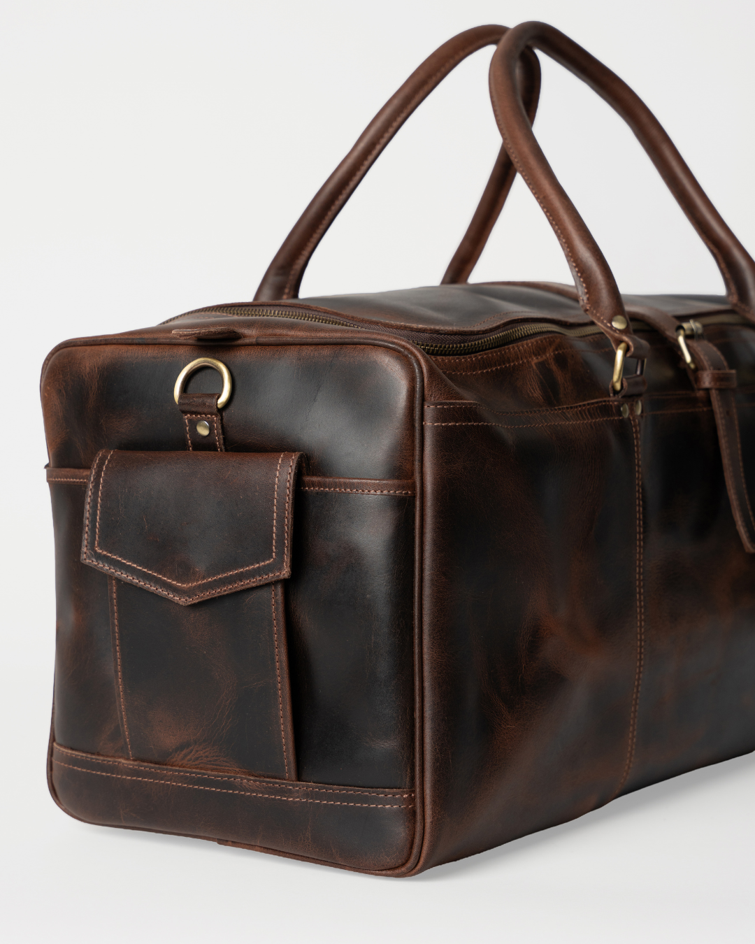 Angled end detail of the Laylowe Holden dark brown leather travel bag showing the flap pocket and strap ring.