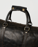 Laylowe Beck dark brown leather duffle close-up showing the snap-fastened handle wrap, metal fittings and top zipper.
