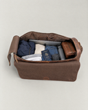 Laylowe Rhodes light brown leather duffle with its flap folded forward, showing clothes, a laptop, passport and bottle inside.