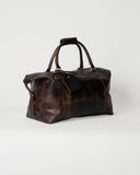 Angled view of the Laylowe Hayes dark brown leather weekender, showing the side buckle and carry handles.