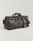 Angled view of the Laylowe Rhodes dark brown leather travel bag showing the end zip pocket, handles and front buckle.