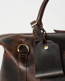 Laylowe Hayes dark brown leather weekender detail showing the luggage tag, handle fitting and shoulder-strap ring.