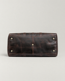Bottom view of the Laylowe Rhodes dark brown leather travel bag showing five metal feet and its stitched leather base.