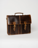 Laylowe Grant brown full-grain leather briefcase with a top handle, flap closure and two buckle straps.