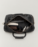 Laylowe Blake black leather duffle open with a laptop, folded clothes, passport, toiletry pouch and steel bottle.