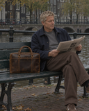 Laylowe Reid brown leather work bag beside a man reading a newspaper on a bench by a canal.
