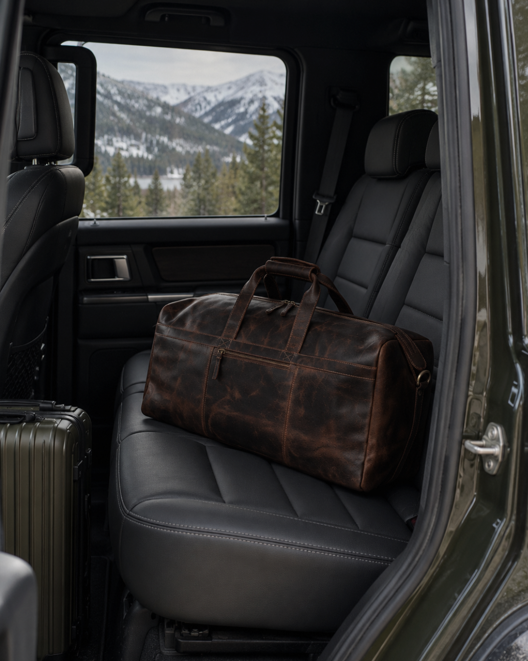 Laylowe Rowan dark brown leather duffle on an SUV rear seat with snowy mountains visible through the window.
