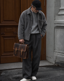 Man holding the Laylowe Grant brown leather briefcase beside a wooden doorway, wearing a gray jacket and trousers.