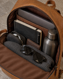 Open Laylowe Lane tan leather backpack packed with a laptop, black journal, pen, dark bottle, sunglasses and folded knitwear.