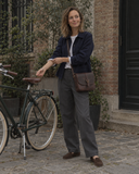 Woman wearing the Laylowe Cora dark brown leather satchel across her body while standing beside a bicycle.