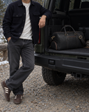 Laylowe Blake black leather duffle in an open SUV trunk beside a man in a dark jacket.