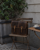 Laylowe Grant brown leather briefcase on a wooden cafe chair beside a table with coffee and a notebook.
