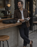 Laylowe Nolan black leather laptop case on an outdoor cafe counter beside a man reading a magazine.
