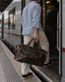 Man boarding a train with the Laylowe Hayes dark brown leather weekender held by its carry handles.