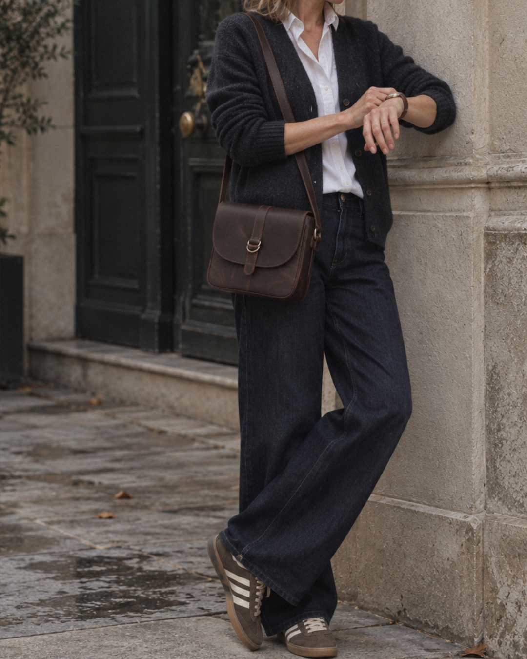 Woman wearing the Laylowe Cora dark brown leather crossbody satchel with a navy cardigan and dark jeans.