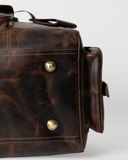 Underside detail of the Laylowe Bennett dark brown leather travel bag showing metal feet and stitched leather panels.