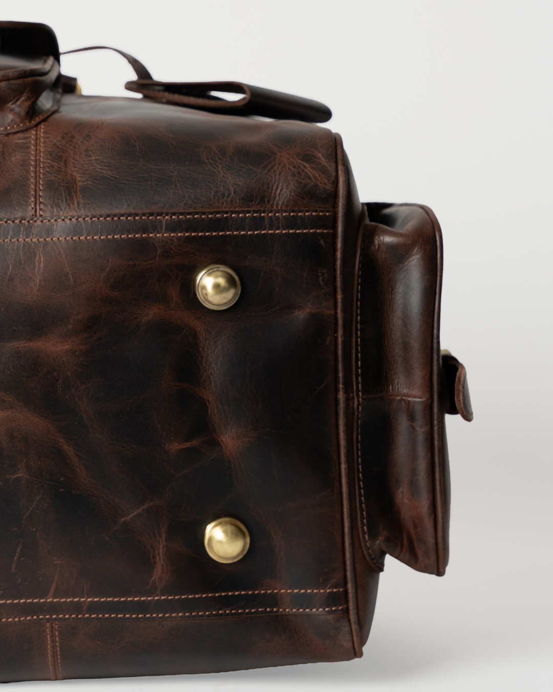 Underside detail of the Laylowe Bennett dark brown leather travel bag showing metal feet and stitched leather panels.