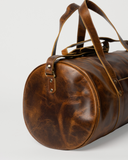 Close-up of the Laylowe Wells light brown leather weekender showing its rounded end, strap ring and stitched handle.