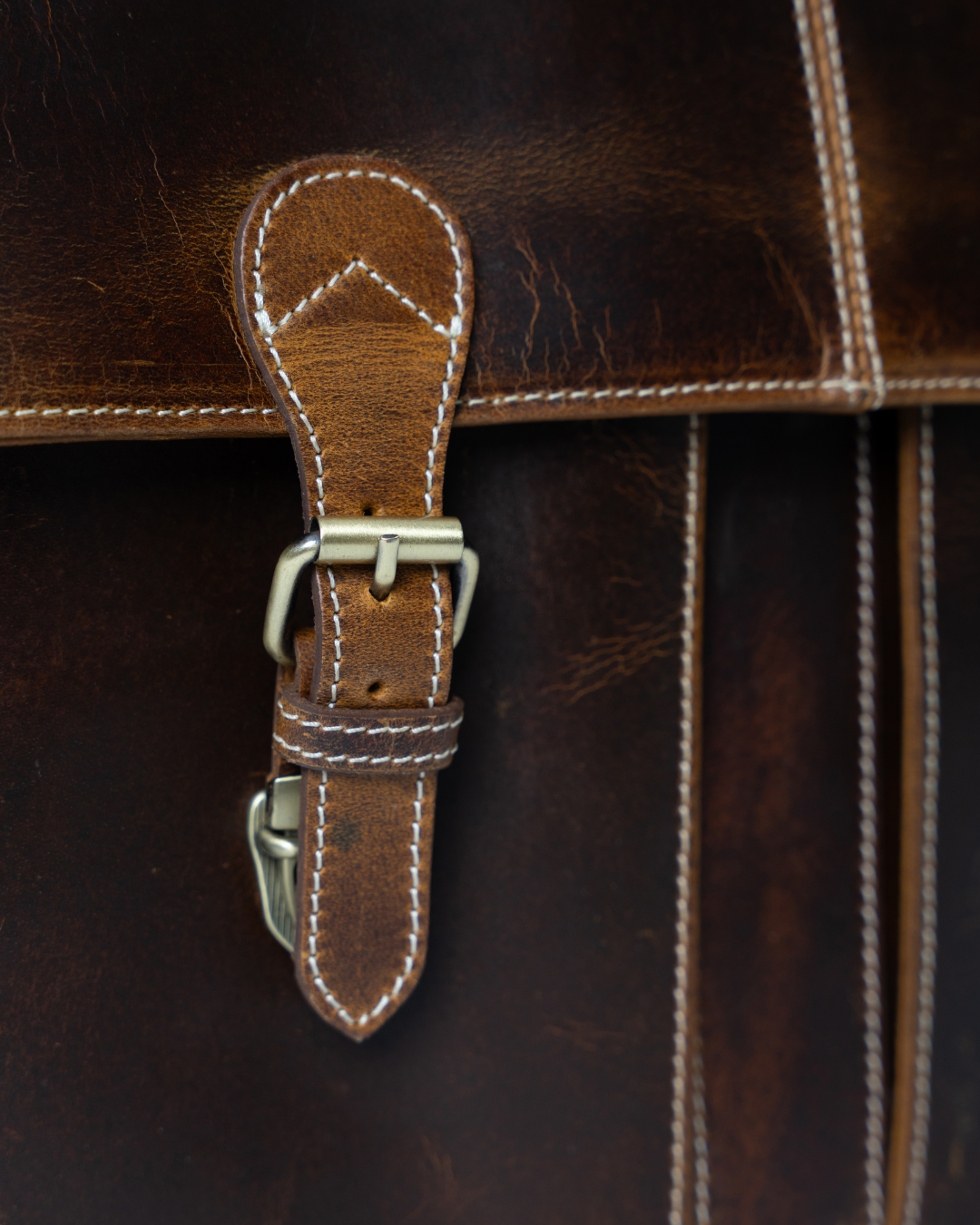 Close-up of the Laylowe Grant brown leather briefcase showing a buckle strap, contrasting stitching and leather texture.