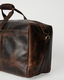 Close-up of the Laylowe Rowan dark brown leather duffle showing its end panel, piping and metal shoulder-strap ring.
