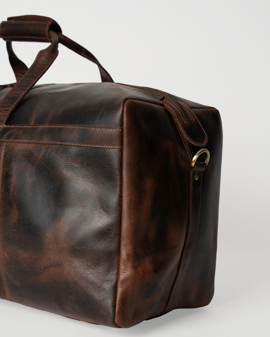 Close-up of the Laylowe Rowan dark brown leather duffle showing its end panel, piping and metal shoulder-strap ring.
