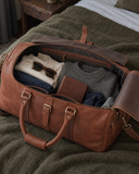Open Laylowe Parker tan leather travel bag on a wool blanket, packed with a shirt, knitwear and sunglasses.