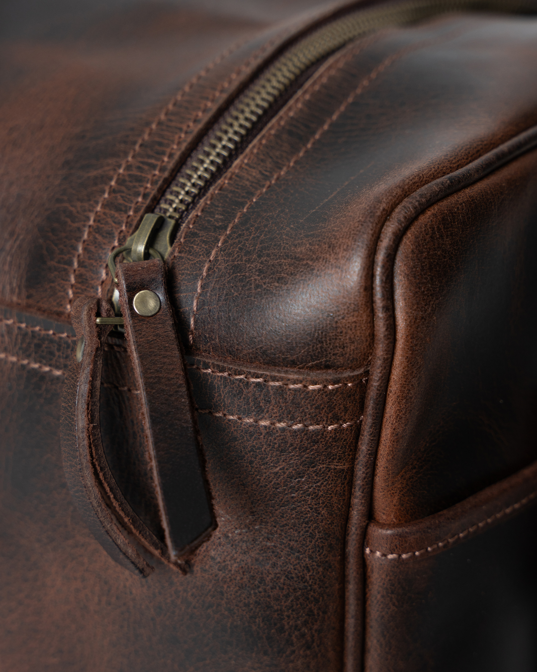 Laylowe Bennett dark brown leather travel bag detail showing a zipper with leather pull, piping and stitching.
