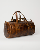 Angled view of the Laylowe Wells light brown leather duffle showing its barrel shape, circular end and carry handles.